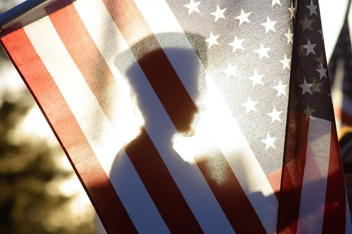 Uniformed Soldier silhoutted by the American Flag
